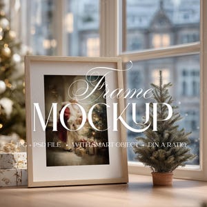May include: A framed image mockup with a Christmas theme. The frame is light wood, and the image inside depicts Santa Claus. A small Christmas tree in a terracotta pot sits on the windowsill. The text "Frame Mockup" is overlaid on the image.