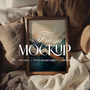 Puede incluir: Una maqueta de marco rectangular de madera con una pintura de paisaje con tonos azules, turquesas y dorados. El marco está apoyado contra almohadas y una manta. El texto "Frame Mockup" se muestra en el marco.