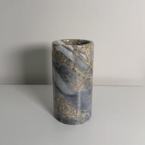 Peut inclure: Un vase cylindrique en marbre avec un motif gris, blanc et doré. Le vase est de couleur unie et a une finition lisse et polie. Le vase mesure environ 13 cm de haut.