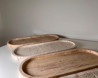 May include: Four oval-shaped decorative trays in varying shades of beige and brown. The trays have a textured, stone-like appearance and are arranged in a row. The trays are made of a natural material and have a smooth, curved edge.