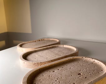 Puede incluir: Tres bandejas ovaladas beige dispuestas sobre una superficie blanca. Las bandejas tienen una superficie texturizada y porosa y un borde ligeramente elevado. Las bandejas están hechas de un material similar a la piedra. Adecuado para la decoración del hogar.