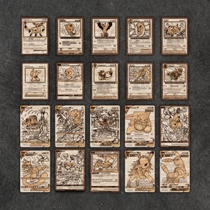 May include: A selection of wooden Pok&eacute;mon trading cards, each featuring a different character and design. The cards are laser-cut with detailed artwork and text. The cards are displayed on a dark surface, showcasing the wooden texture.