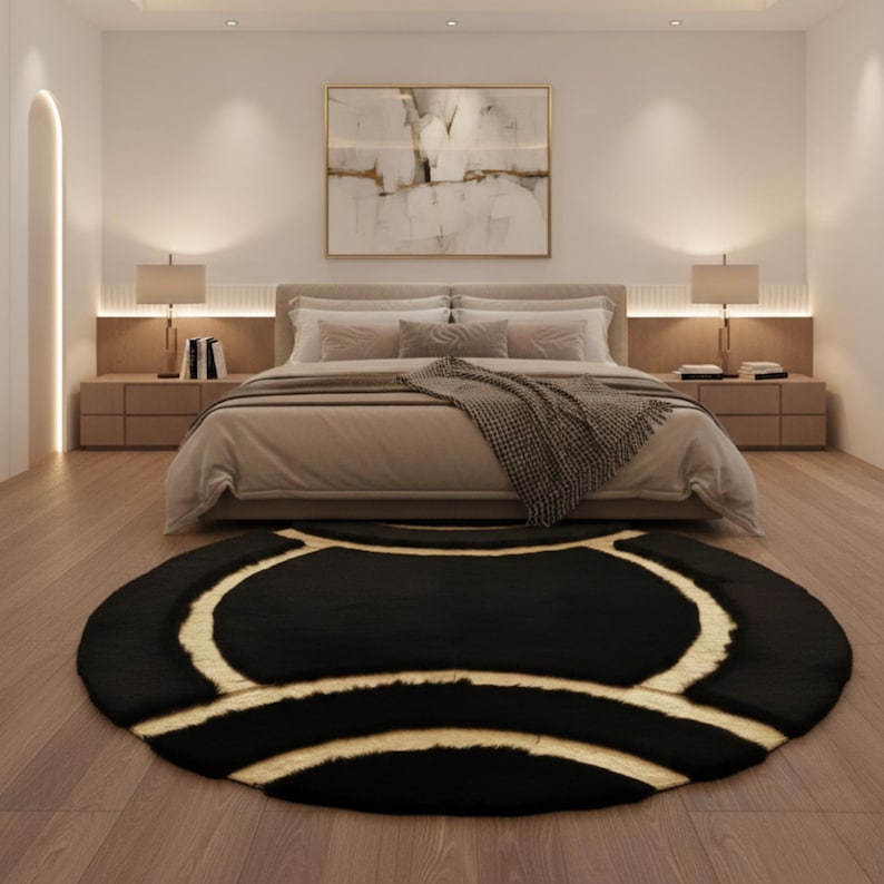 May include: A black and beige round rug with a geometric design is centered in front of a bed. The rug has a dark, textured surface with beige curved lines. The bedroom features a neutral color palette with a large painting and lamps.
