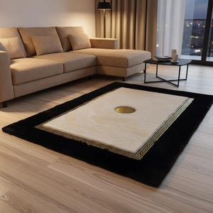 May include: A rectangular area rug with a black border and a cream-colored center. The rug features a gold Greek key design and a circular gold accent in the center. The rug is placed on a light wood floor.