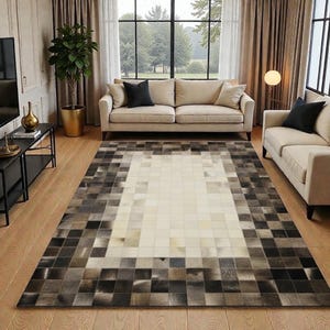 Puede incluir: Una alfombra rectangular con un patrón geométrico en tonos crema, gris y marrón. La alfombra presenta una sección central de color crema rodeada por un borde de cuadrados en diferentes tonos de gris y marrón. La alfombra está colocada sobre un suelo de madera.
