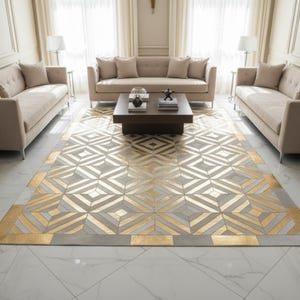 May include: A large area rug with a geometric pattern in gold, gray, and white tones. The rug is rectangular and features a repeating design of diamonds and lines. The rug is placed in a living room setting with beige sofas and a dark brown coffee table.