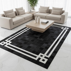 Può includere: Un moderno salotto con un tappeto a motivi geometrici in bianco e nero. Il tappeto è posizionato davanti a due divani beige e un tavolino in legno chiaro. Vasi e libri sono sul tavolo.