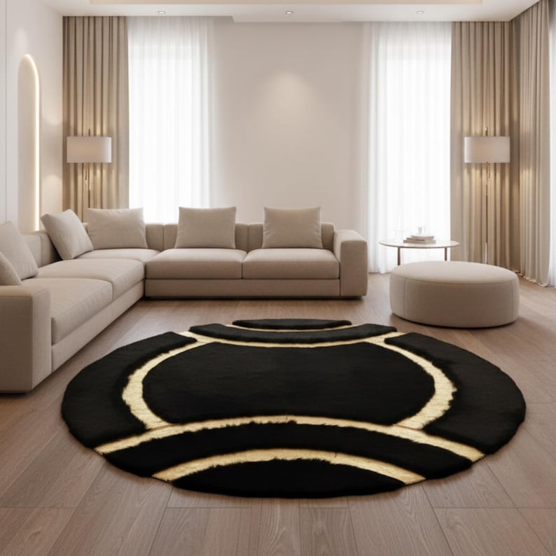 May include: A black and beige round area rug with a unique design. The rug features a black background with beige curved lines and shapes. The rug is placed on a hardwood floor in a living room setting.