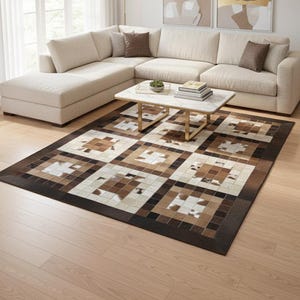 Può includere: Un tappeto rettangolare con un motivo geometrico nei toni del marrone, beige e bianco. Il tappeto è posizionato su un pavimento in legno chiaro. Sullo sfondo un divano angolare beige e un tavolino bianco.