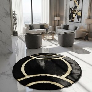 May include: A black and gold area rug with a circular design. The rug features a black background with gold-colored curved lines and geometric shapes. The rug is placed on a white marble floor in a modern living room setting.