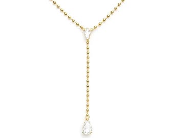 May include: A delicate gold-colored necklace with a Y-shaped design. The necklace features a chain of small beads and two pear-shaped, clear gemstones. The gemstones are suspended from the chain, creating a simple yet elegant look.