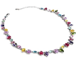 Può includere: Una collana d'argento con una varietà di pietre preziose colorate di diverse forme. Le pietre preziose includono tonalità rosa, viola, gialle, verdi e blu. La collana è un gioiello delicato.