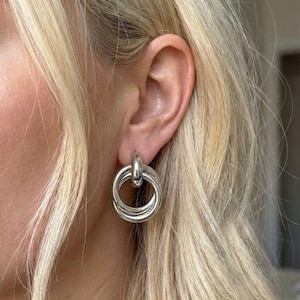 Puede incluir: Pendientes de aro plateados con un diseño de múltiples anillos. Los pendientes tienen un acabado pulido y un cierre de poste. Un accesorio clásico para el uso diario.