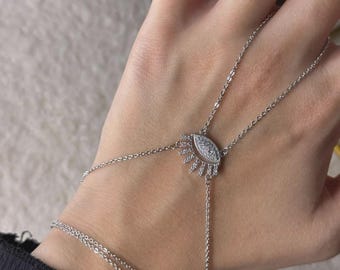 May include: A silver hand chain bracelet featuring an eye-shaped charm with clear, sparkling stones. The bracelet connects to a finger ring with a delicate chain. The design includes a double-strand bracelet that wraps around the wrist.