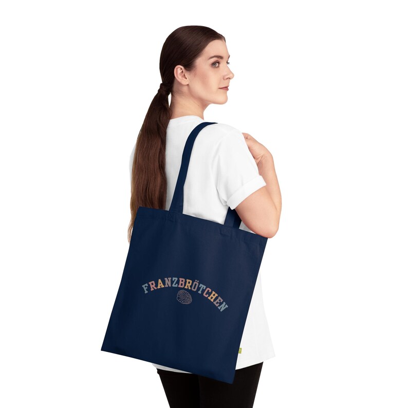 May include: A navy blue tote bag featuring the word "FRANZBR&Ouml;TCHEN" in a multi-coloured arched font. Below the text is a pastry graphic. The bag is carried over the shoulder.