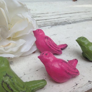 May include: Four small bird figurines, two are pink and two are green. The birds are painted in a distressed style and have a rustic look.