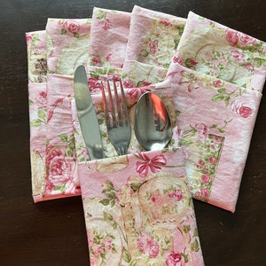 May include: Four pink fabric napkin holders with floral patterns, each holding a fork, knife, and spoon.