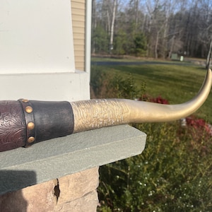 May include: A gold-painted bull horn with a brown leather and black wood base. The base has decorative stitching and brass studs.