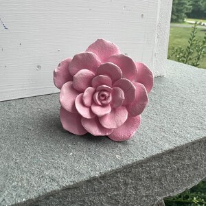 Peut inclure: Une fleur en céramique rose avec une surface texturée. La fleur a plusieurs couches de pétales et un petit centre.