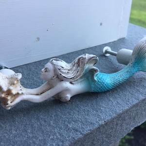 May include: White ceramic mermaid door knob with a blue tail and a seashell in her hand.