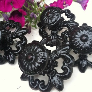 May include: Four black metal cabinet knobs with ornate designs. The knobs have a shiny, polished finish.