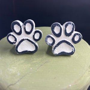 May include: Two white ceramic paw print ornaments with black outlines. The paw prints are about 2 inches in diameter.