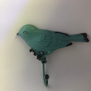 May include: A turquoise blue bird shaped wall hook with a black eye and a black tail. The hook is made of metal and has a rustic finish.