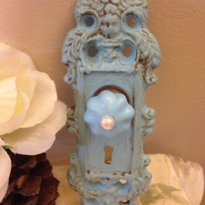 May include: A light blue decorative door knob with a white porcelain knob and a keyhole. The knob is ornate and has a distressed finish.