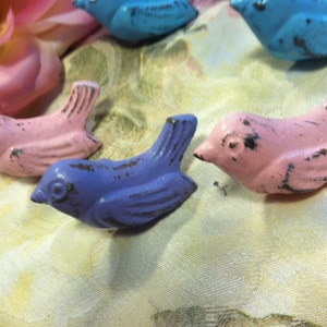 Może przedstawiać: Pięć małych, metalowych gałek do szuflad w kształcie ptak&oacute;w w kolorze r&oacute;żowym, niebieskim i fioletowym z wykończeniem w stylu vintage.