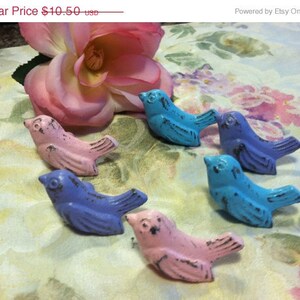 Może przedstawiać: Sześć małych, ptasich uchwyt&oacute;w do szuflad w r&oacute;żnych odcieniach niebieskiego i r&oacute;żowego. Uchwyty są postarzone i mają vintage'owy wygląd.