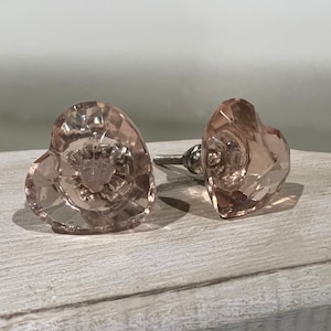 May include: Two pink glass heart-shaped cabinet knobs with a faceted design.