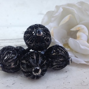 May include: Four black metal cabinet knobs with a delicate, intricate design. The knobs are round and have a slightly raised center.