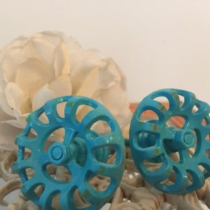 May include: Two turquoise blue metal cabinet knobs with a decorative, circular, openwork design. The knobs have a rustic, vintage look.