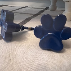 May include: Two blue paw print cabinet knobs with a silver metal connecting rod.