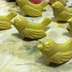 Peut inclure: Une collection de neuf petites figurines d'oiseaux en c&eacute;ramique jaune. Les oiseaux sont tous tourn&eacute;s dans la m&ecirc;me direction et ont un design simple et arrondi.