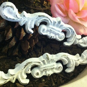 Peut inclure: Deux poignées de tiroir en métal blanc ornées, avec une finition vieillie. Les poignées sont dans un décor rustique avec des pommes de pin et de la terre.