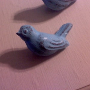 May include: A light blue ceramic bird figurine with a distressed finish. The bird has a long tail and a small beak.