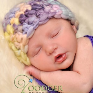 Peut inclure: Un bébé endormi portant un bonnet crocheté multicolore et une tenue violette. Le bébé est allongé sur une surface blanche et moelleuse. Le texte "www.calleightsclips.com" est visible dans le coin supérieur gauche de l'image.