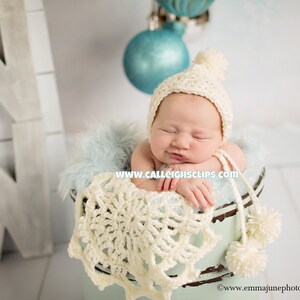May include: A sleeping baby wearing a white crocheted hat in a blue and white crocheted bucket with a white snowflake design.