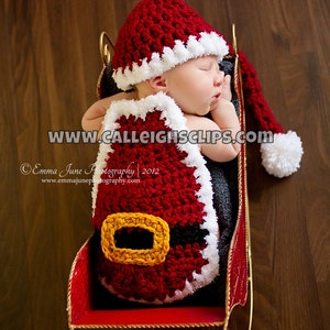 Könnte beinhalten: Ein Baby in einem rot-weißen gehäkelten Weihnachtsmannkostüm mit schwarzem Gürtel, das in einem roten Schlitten mit goldenen Verzierungen schläft. Das Bild enthält den Text "www.calleightsclips.com".