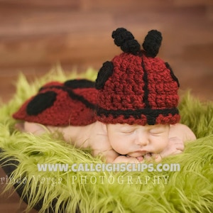 Puede incluir: Un bebé recién nacido con un gorro de crochet de mariquita rojo y negro y un disfraz de mariquita a juego, durmiendo en una cama de piel verde.