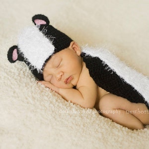 Könnte beinhalten: Ein neugeborenes Baby trägt ein schwarz-weißes Stinktierkostüm mit einem flauschigen Schwanz. Das Baby schläft auf einer weißen, flauschigen Decke.