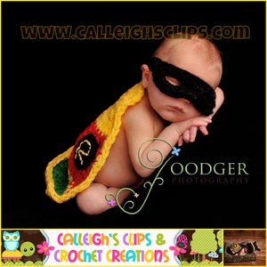 Puede incluir: Un bebé recién nacido con un disfraz de Robin de crochet con una capa amarilla, roja y verde y una máscara negra para los ojos. El bebé está durmiendo con la cabeza apoyada en el brazo. La imagen incluye el texto "www.calleightsclips.com" y "Oodger Photography".