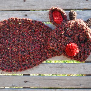 Könnte beinhalten: Ein gehäkeltes Rentier-Ornament in Braun-, Rot- und Weißtönen. Das Rentier hat eine rote Pompon-Nase und geschlossene Augen.