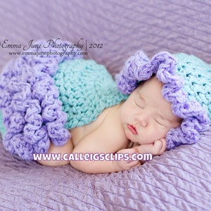 May include: A sleeping baby wearing a purple and turquoise crocheted hat and matching outfit. The baby is lying on a purple textured blanket.