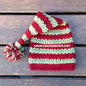 May include: Red and green striped crocheted hat with a long, pointed top and a pom-pom on the end. The hat has a website address on the side: www.calleightsclips.com