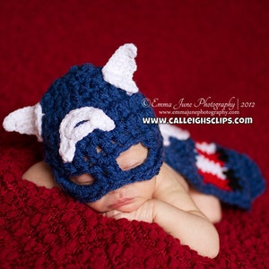 May include: A baby wearing a blue and white crocheted Captain America costume, sleeping on a red textured blanket. The costume features a hat with a mask and a matching cape. The text "Emma June Photography | 2012 www.emmajunephotography.com www.calleightsclips.com" is visible in the background.