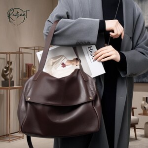 May include: A dark brown leather shoulder bag with a flap closure and a long strap. The bag is held by a person wearing a gray coat. The word "Radiant" is visible in the upper left corner.