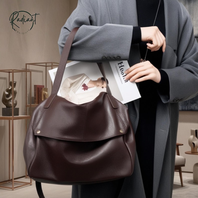 May include: A dark brown leather shoulder bag with a flap closure and a long strap. The bag is held by a person wearing a gray coat. The word "Radiant" is visible in the upper left corner.