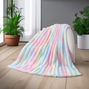 Peut inclure: Une couverture douce aux couleurs pastel avec un motif tie-dye dans les tons de rose, bleu, jaune et blanc. La couverture est drapée sur une chaise blanche. Le mot "Radiant" est dans le coin supérieur gauche.